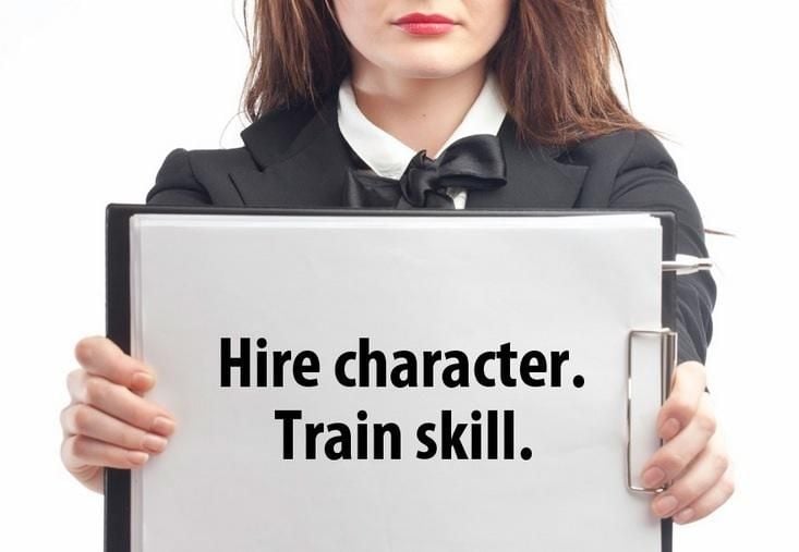woman holding a sign that says Hire character, train skill
